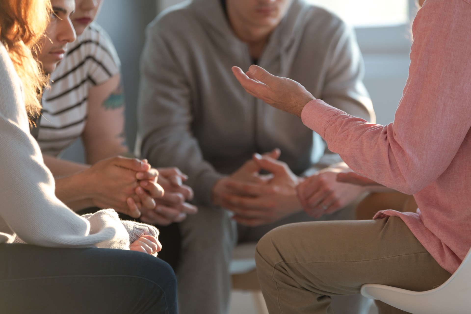 Close-up of a therapist gesticulating while talking to a group of listing teenagers during an educational self-acceptance and motivation meeting.