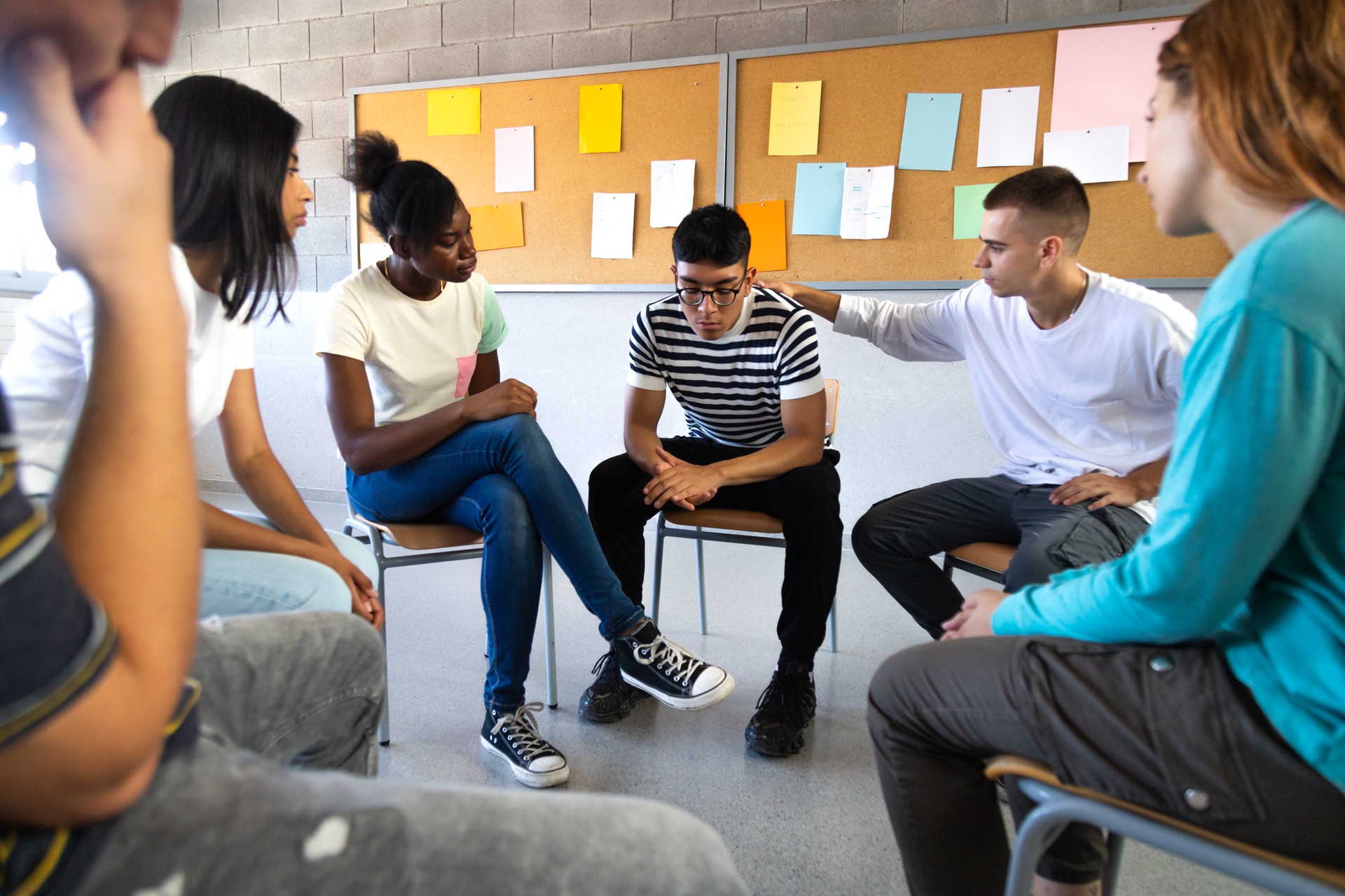 Sad hispanic male high school student sharing bad news with classmates. Multiracial teenagers sitting in circle in